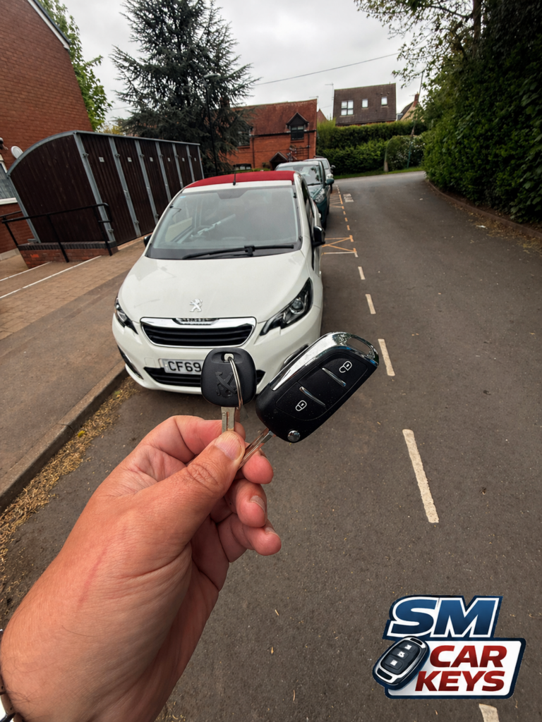 Original and additional Peugeot 108 car keys held in front of a white Peugeot 108 after spare key cutting and programming by SM Car Keys.